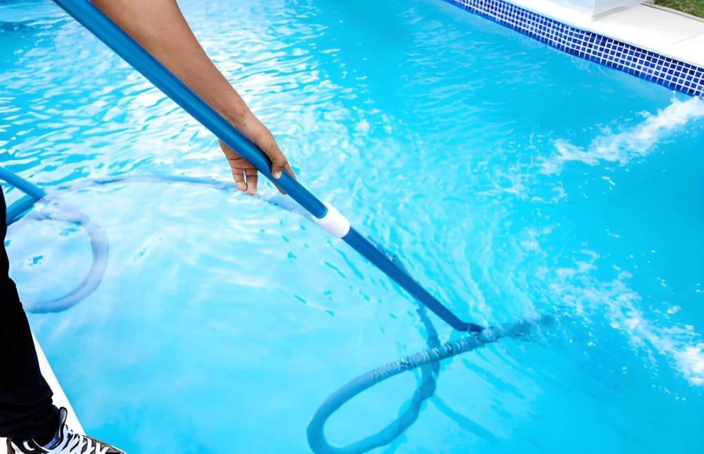 Pool cleaning service Port St Lucie professional using vacuum pole to clean clear blue swimming pool