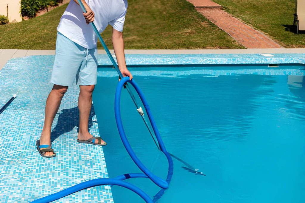 Hobe Sound Pool Service technician cleaning residential swimming pool with vacuum hose and pole.