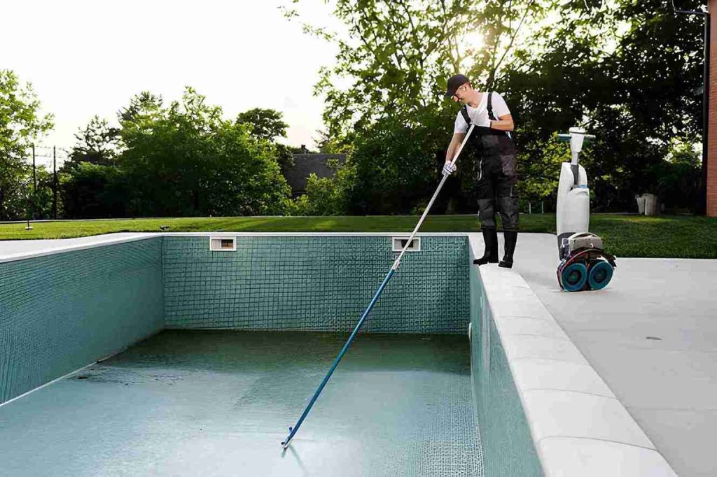 Pool cleaning service Stuart FL worker brushing empty tiled pool with professional equipment.
