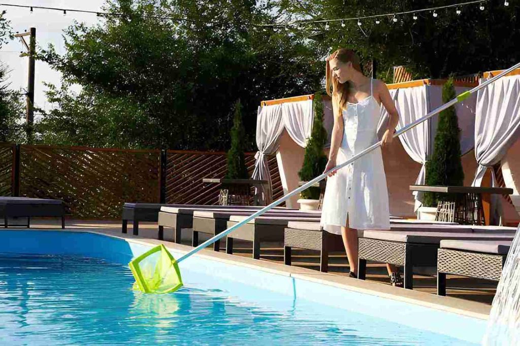Pool cleaning service Port St. Lucie professional using net to clean outdoor pool near cabanas.