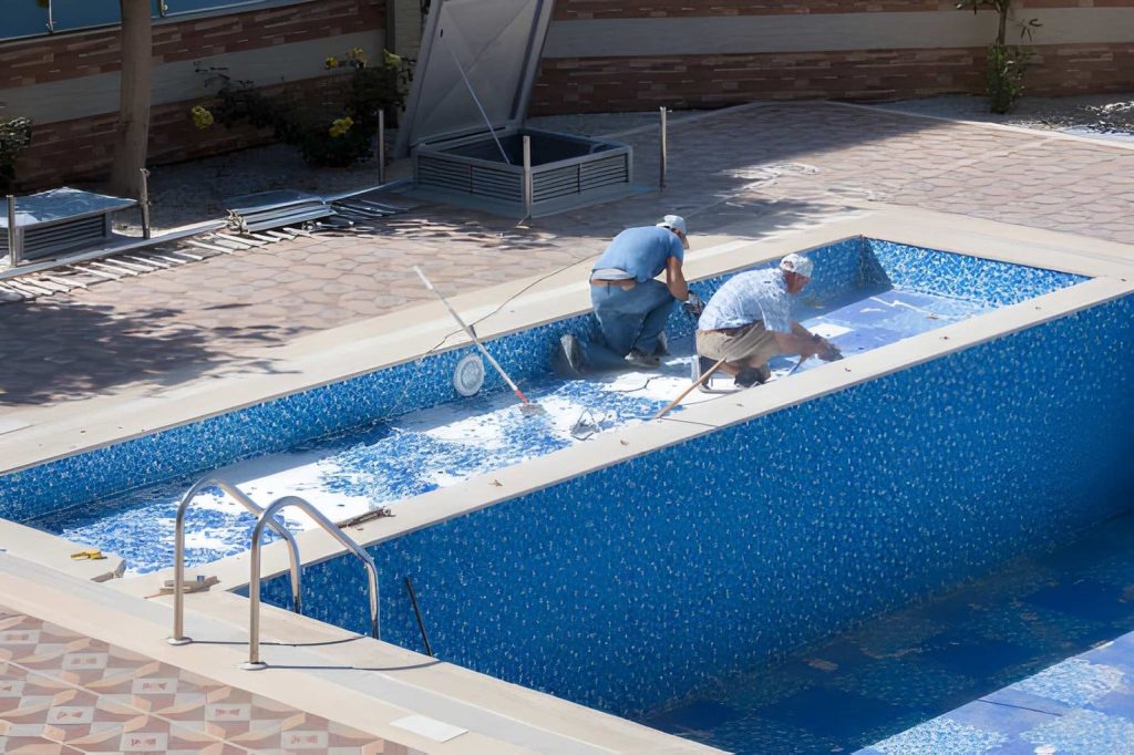 Pool maintenance South Florida workers repairing and installing tiles inside empty swimming pool.