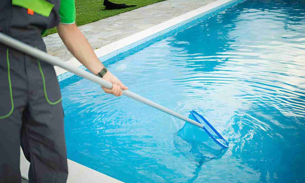 Hobe Sound pool service worker using a blue skimmer net to clear debris from a clear swimming pool.