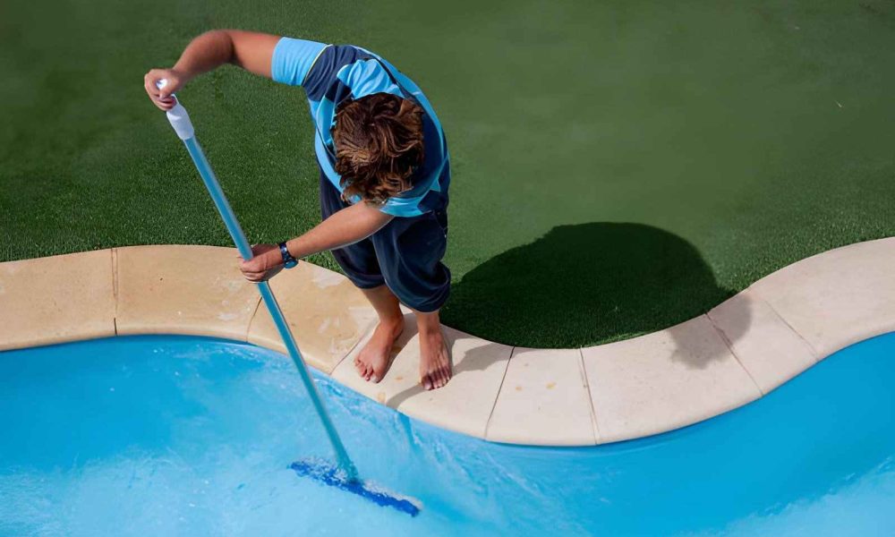 Pool cleaning and maintenance service Jensen Beach professional brushing pool water with long pole beside turf deck
