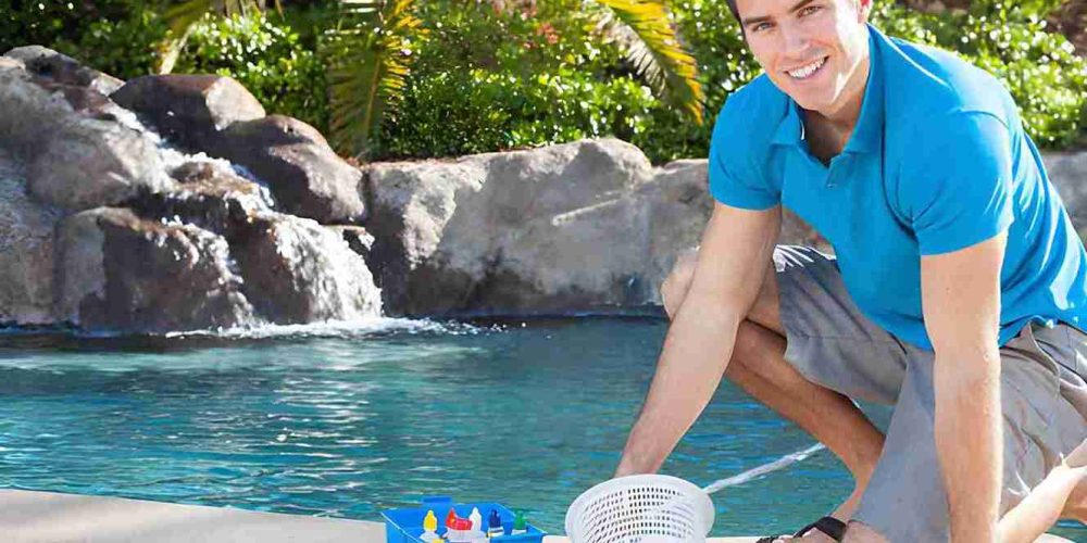 Pool cleaning and maintenance service Jensen Beach professional inspecting skimmer basket and testing water quality beside landscaped pool with waterfall