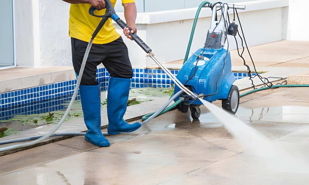 Pool cleaning service Stuart FL professional using pressure washer to clean outdoor tiled poolside area.