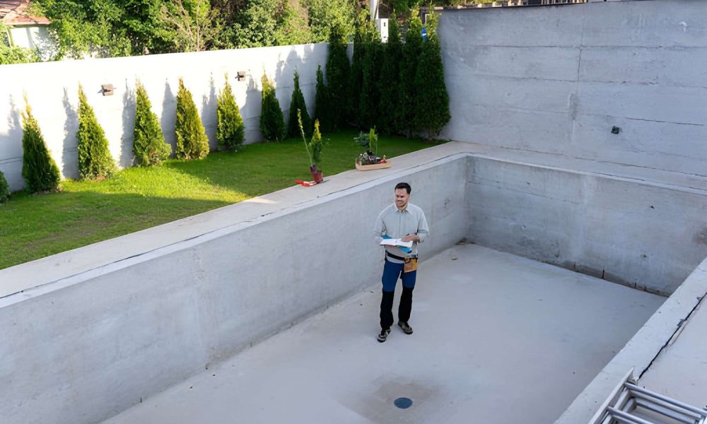 Pool Contractors Port St Lucie FL inspector reviewing blueprints inside unfinished concrete swimming pool.