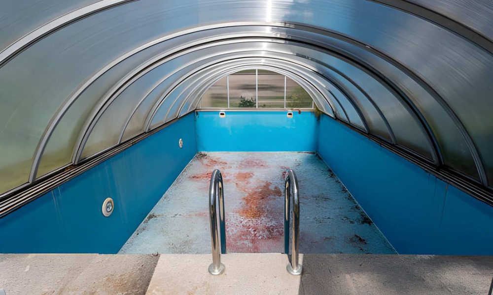 Pool enclosure repair Jensen Beach FL empty covered swimming pool with blue interior and metal handrails.