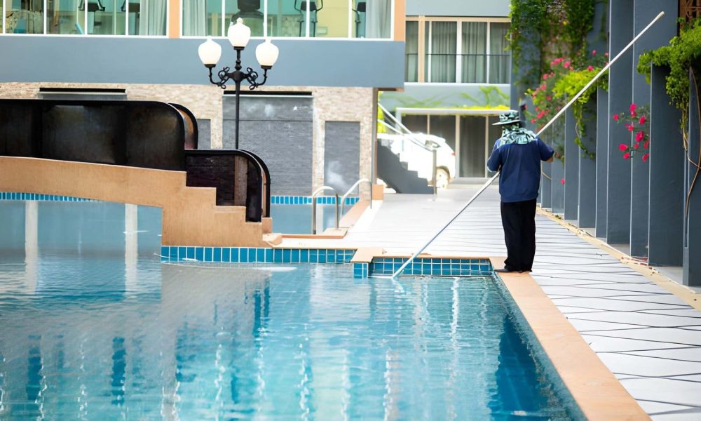 Pool maintenance Stuart FL professional cleaning clear blue pool with long pole net in modern apartment complex