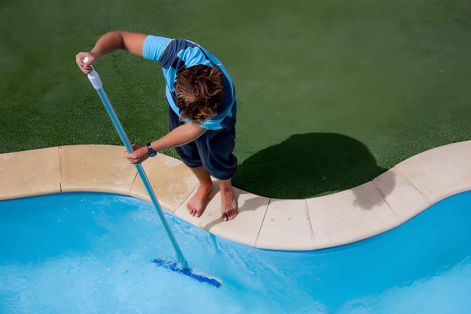 Pool cleaning and maintenance service Jensen Beach professional brushing pool water with long pole beside turf deck