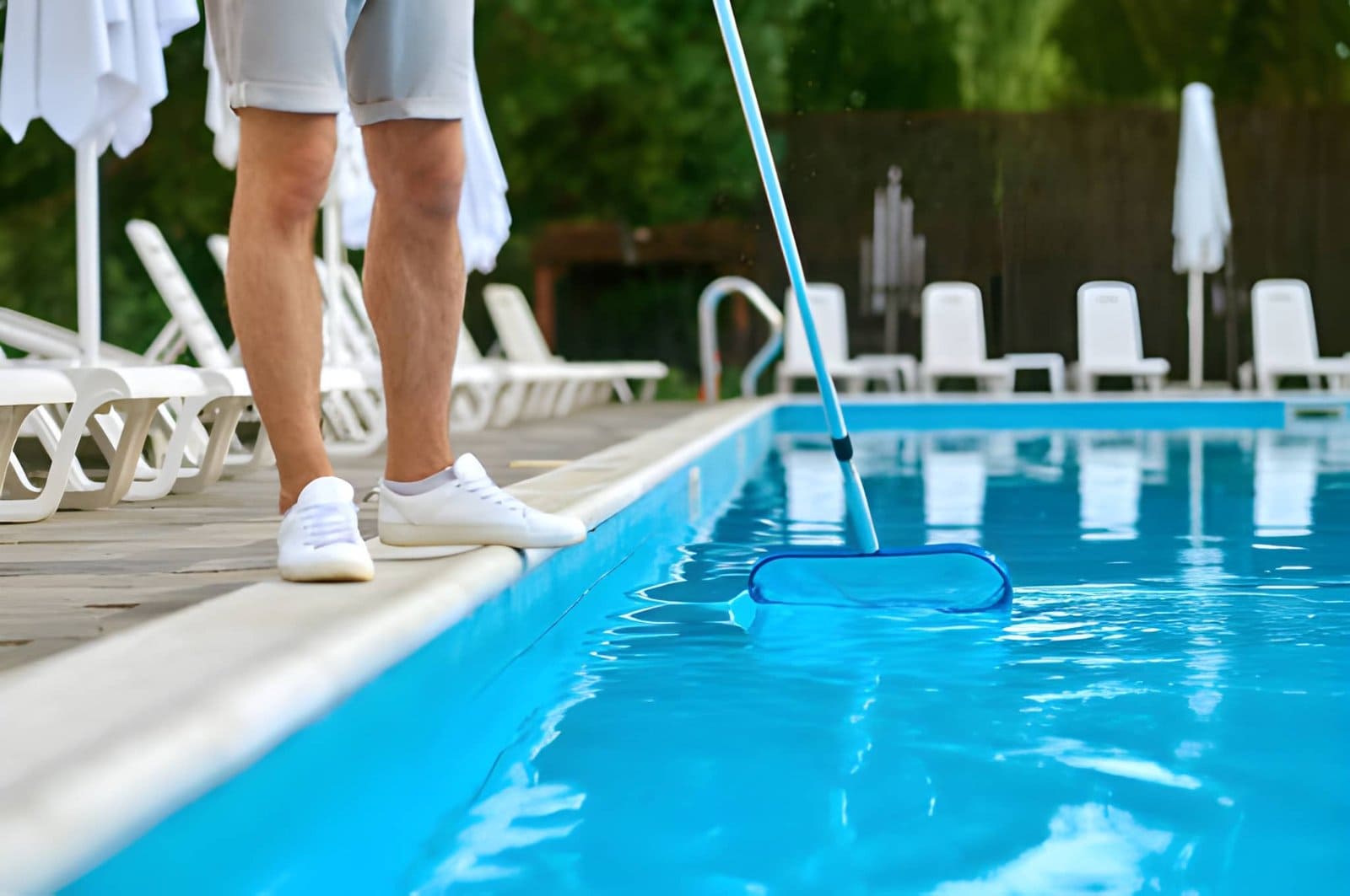 Pool maintenance Port St Lucie FL professional skimming pool water surface with long-handled net near lounge chairs
