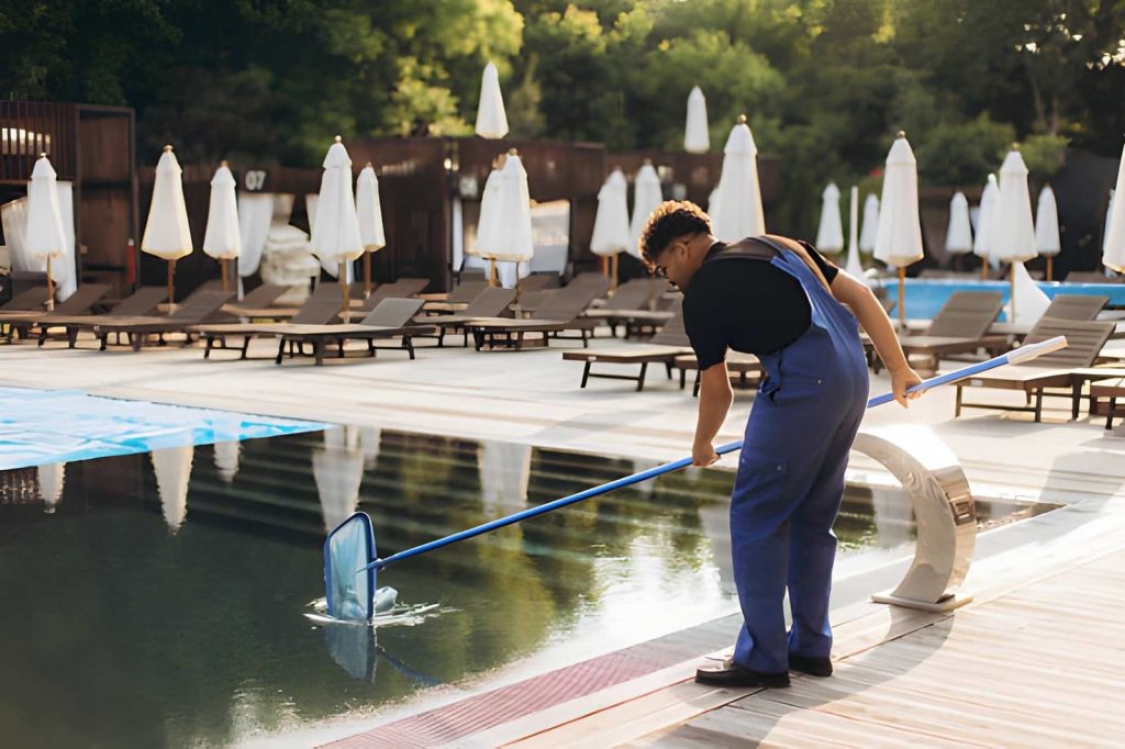 Cleaning pool service Jensen Beach professional using long net pole to remove debris from resort swimming pool.