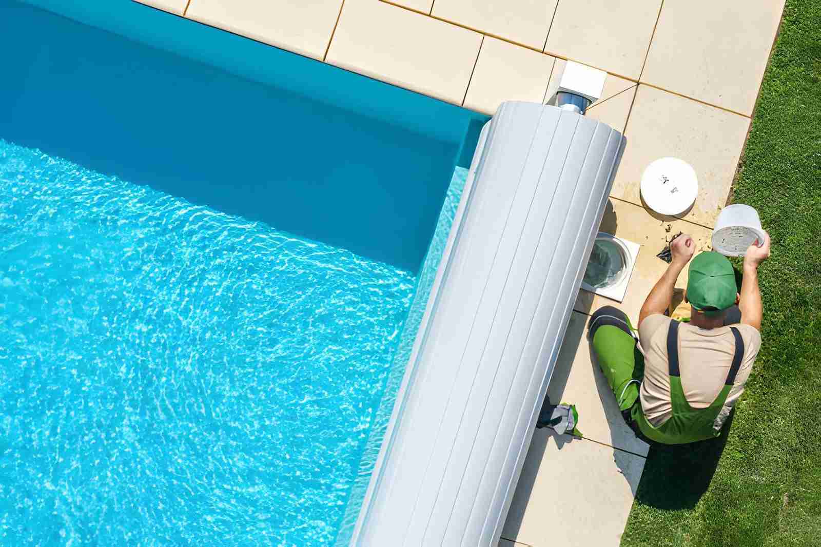 Pool maintenance Port St Lucie technician in green overalls servicing filtration system beside clear blue swimming pool.