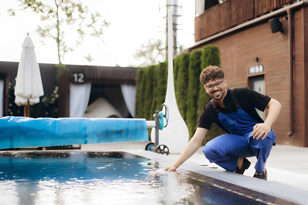 Pool service Stuart technician in blue overalls inspecting clear water at modern outdoor swimming pool.